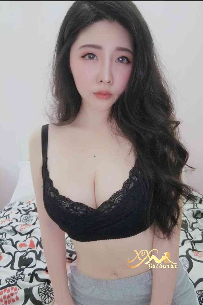 Beautiful Asian woman in black lace bra on bed with patterned sheets.