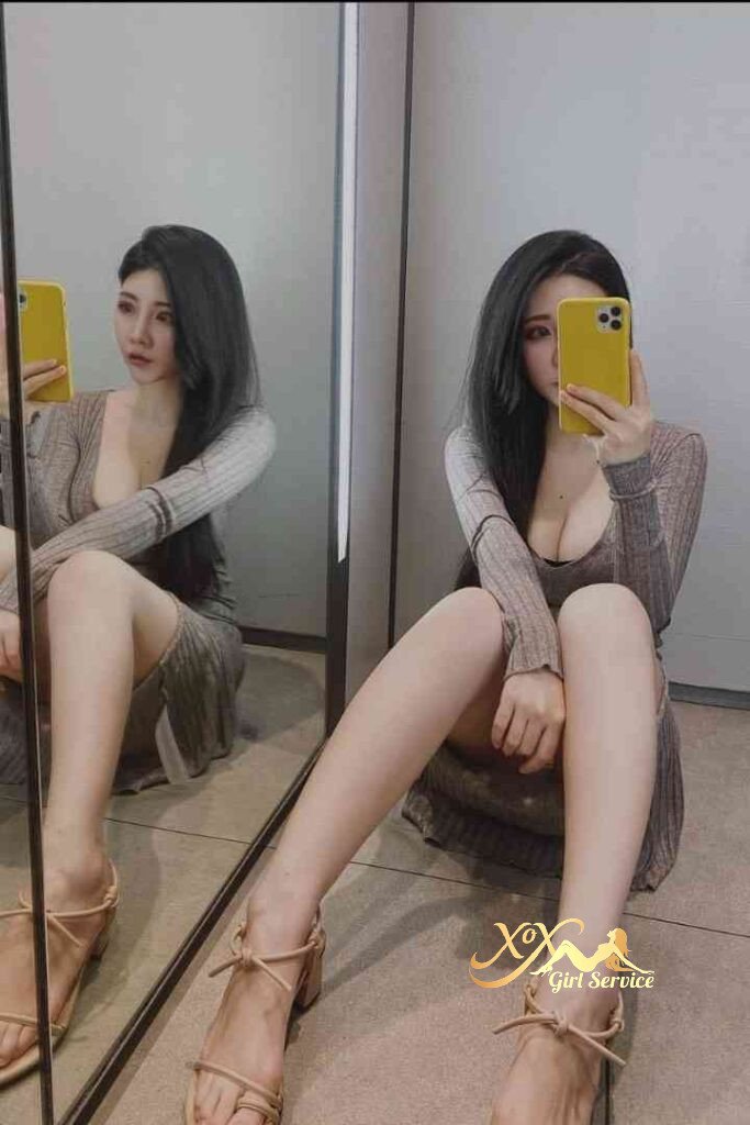 Asian woman in dress sitting near mirror, holding phone. C cup.