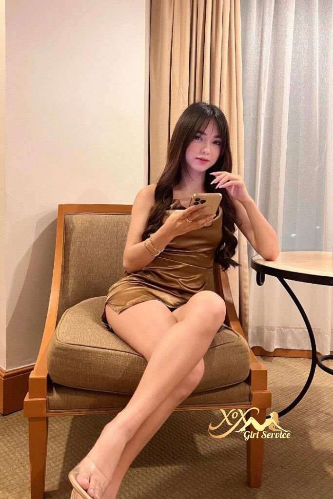 Asian woman in gold dress sitting, holding phone. Tudung Hijab girl.