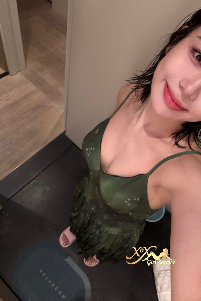 Attractive Asian woman in green dress, pink sandals, and wet hair smiles at the camera.