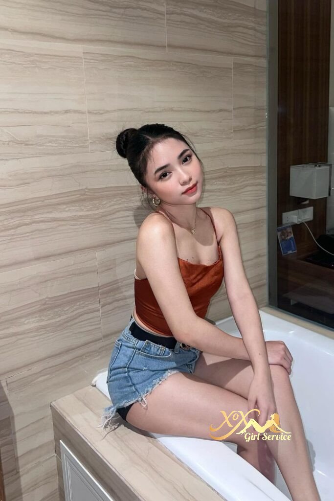 Pretty Asian woman in top and shorts sitting on tub edge.