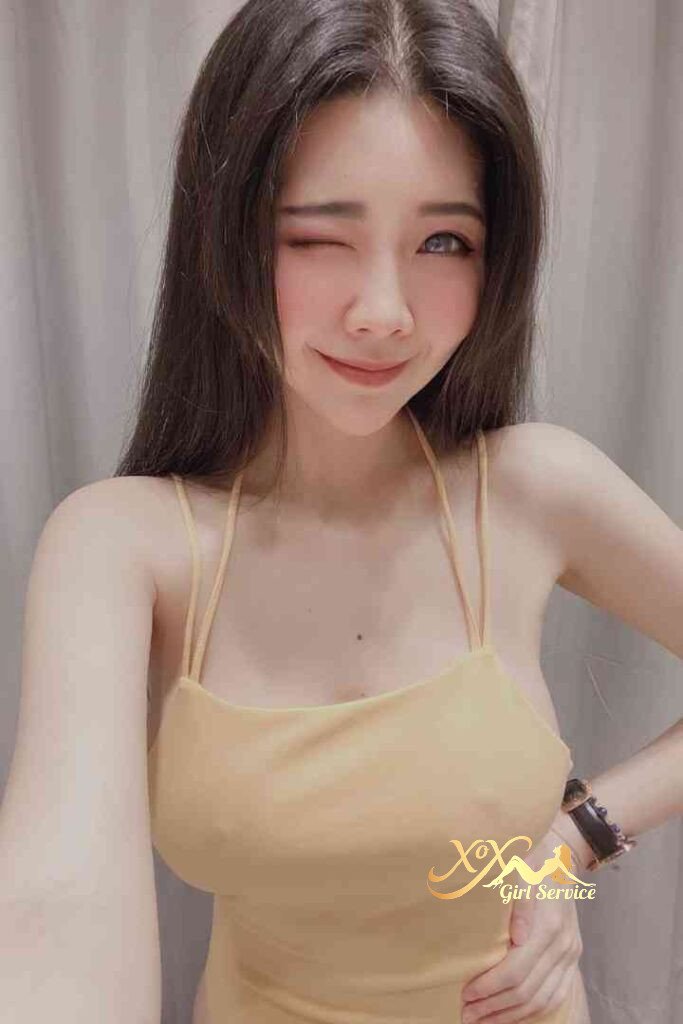 Smiling Asian woman winking in yellow top. KL escort Mei Qing.