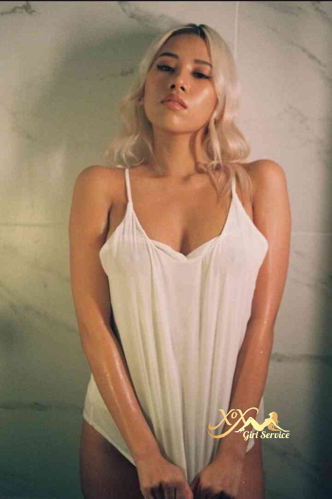 Bella, Thai D cup escort in KL, poses in a white top with wet skin in a bathroom setting.