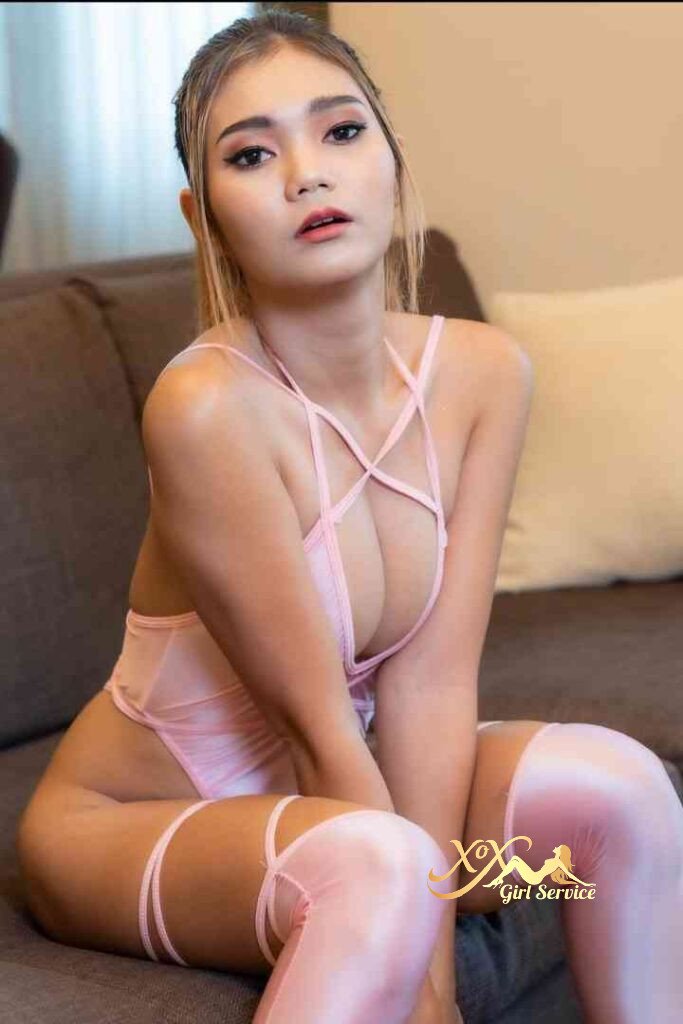 Petite Thai model Vicky in pink lingerie sitting on a couch.