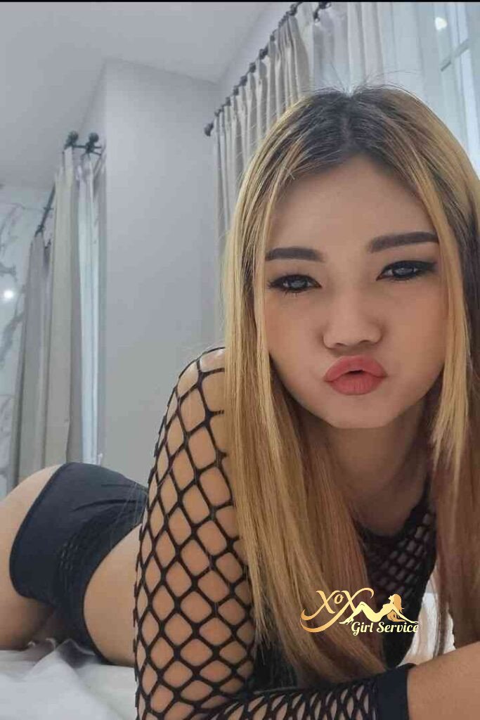 Petite Thai woman in fishnet top and black shorts posing seductively.