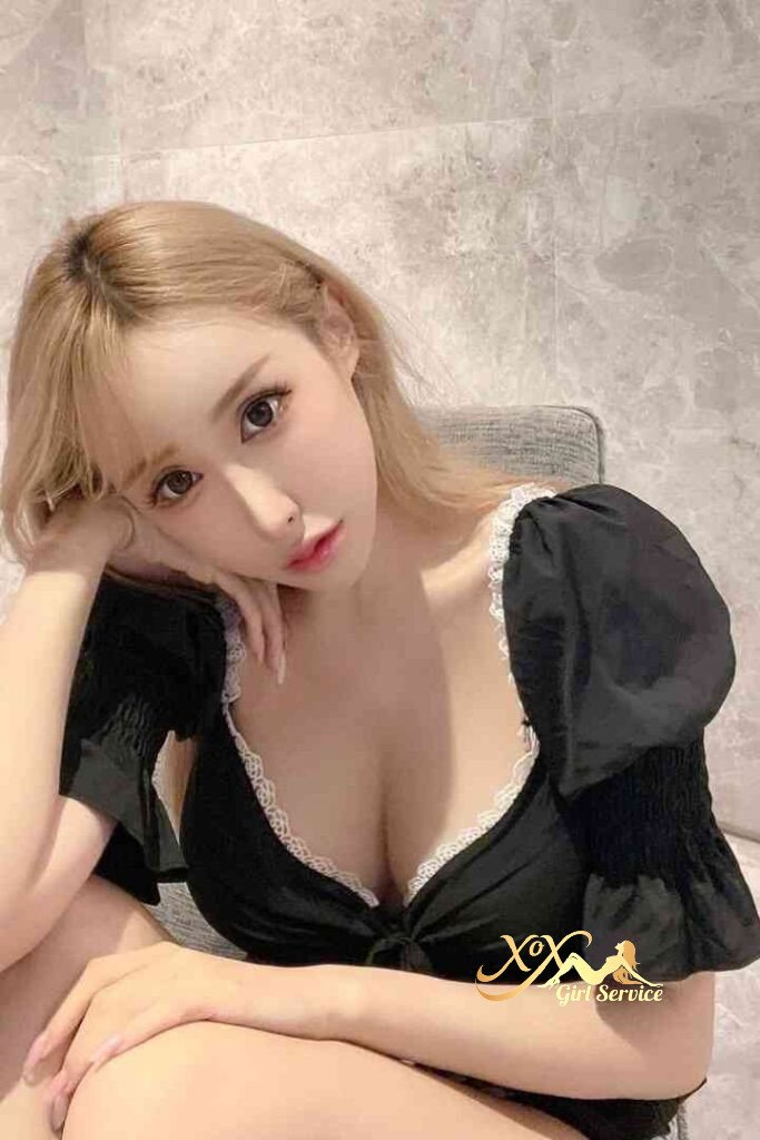 Sexy Vietnamese escort with blonde hair in black top with lace trim, posing seductively.