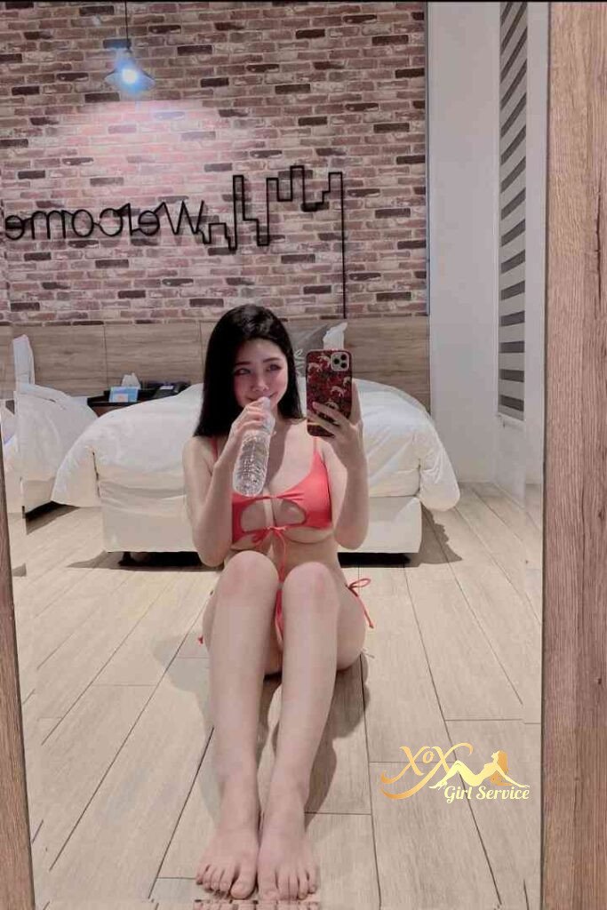 Woman in bikini drinking water, sitting indoors. Mei Qing escort.