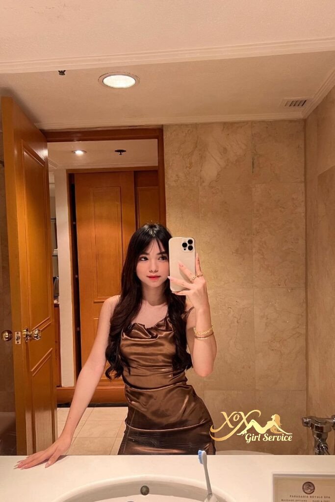 Woman in brown dress takes bathroom mirror selfie. KL Malay escort.